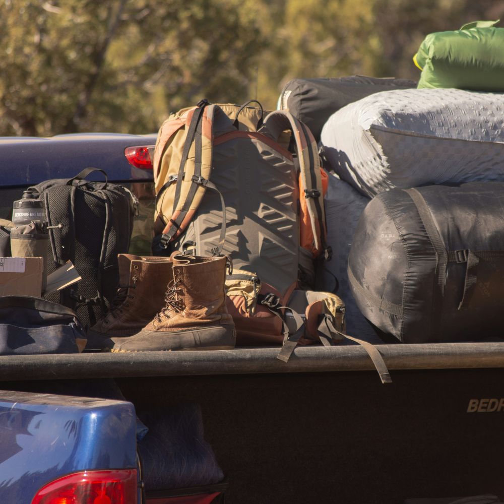 Camping gear, a backpack and boots piled in the back of a pickup truck