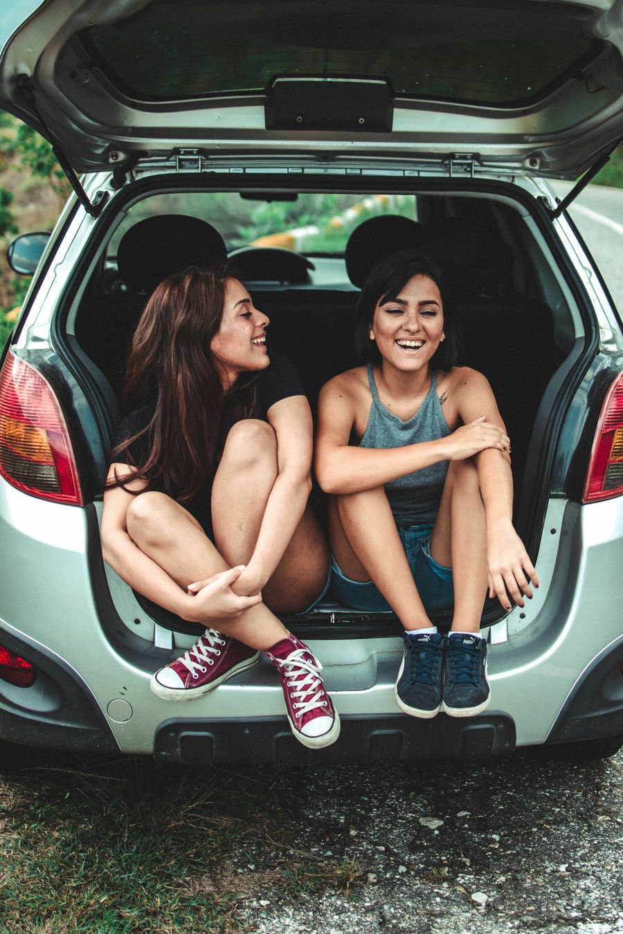 Two friends laughing in the open boot of a hatchback